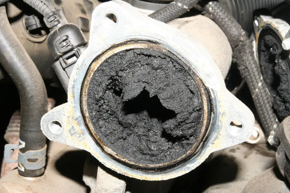 Gros amas de suie noire obstruant une vanne EGR encrass&eacute;e, signe d'un moteur diesel n&eacute;cessitant un nettoyage.