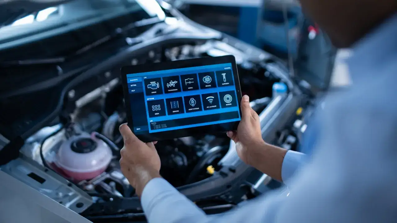 Un m&eacute;canicien utilise une tablette pour diagnostiquer une voiture qui ne d&eacute;marre pas. L'&eacute;cran affiche les syst&egrave;mes du v&eacute;hicule.