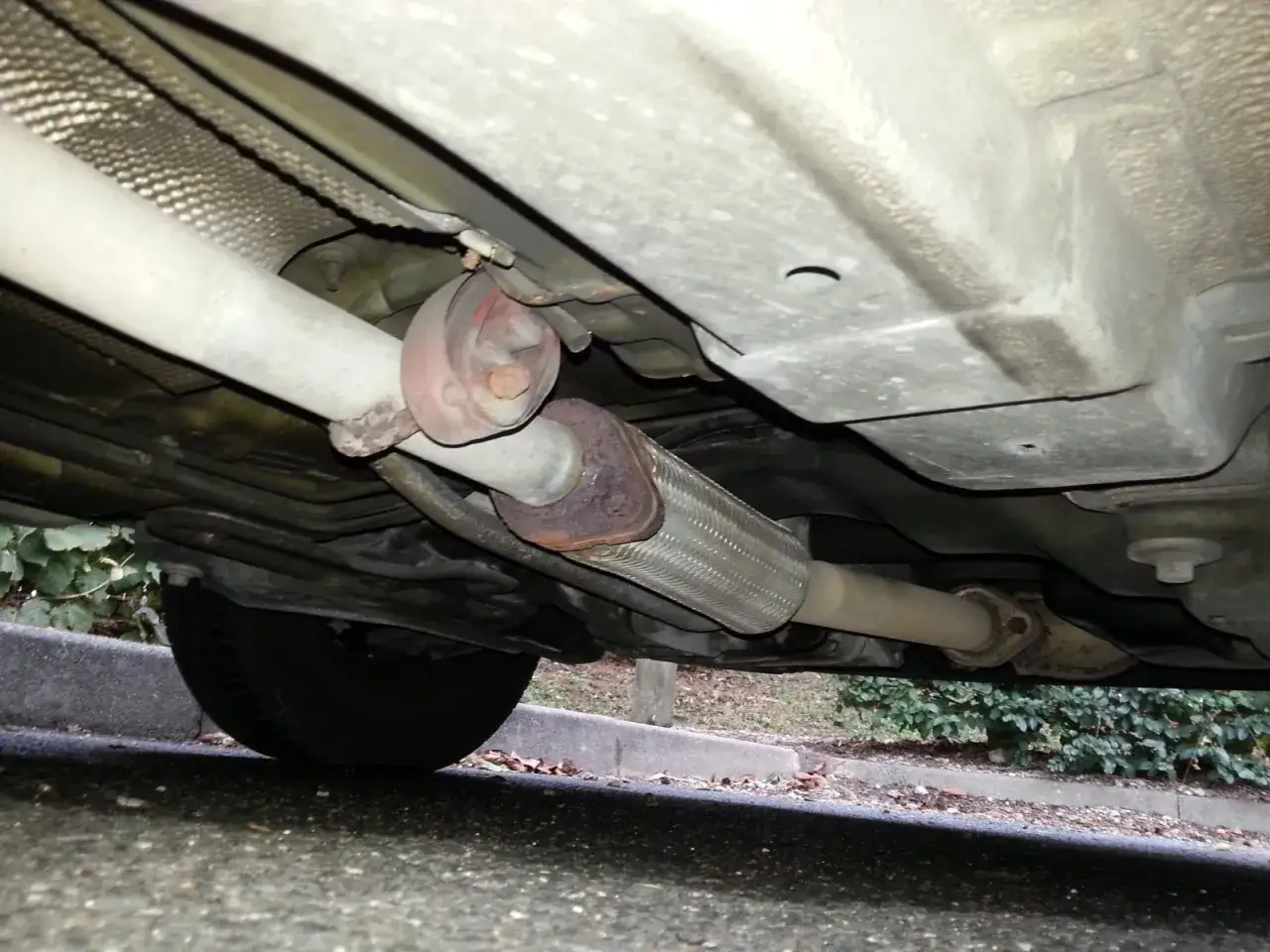 Le dessous d'une voiture, montrant le système d'échappement endommagé. Rouler sans pot d'échappement est bruyant et polluant.