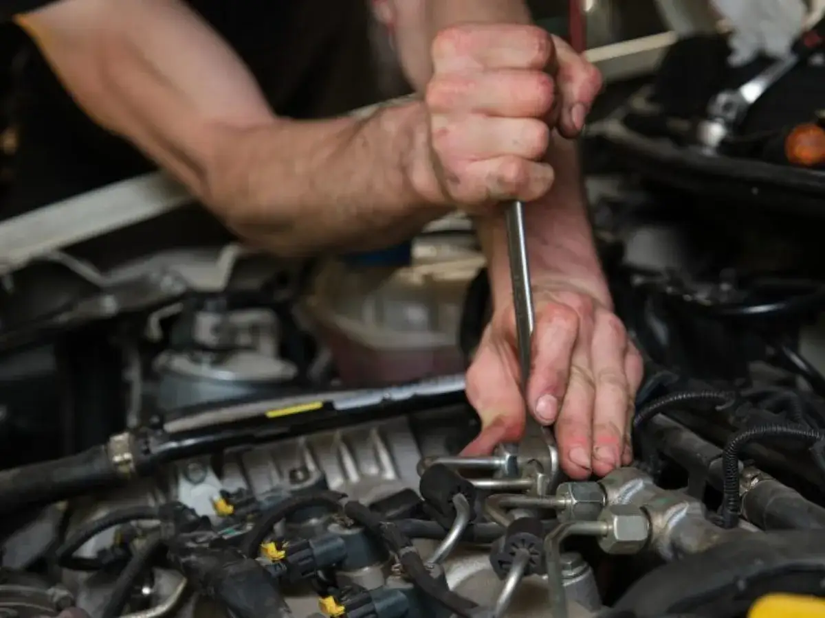 Mains d'un mécanicien travaillant sur un moteur de voiture avec un outil.