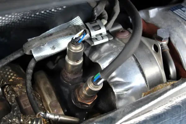 Deux sondes lambda rouillées, un symptôme de sonde lambda défectueuse, sont visibles sous un blindage thermique.