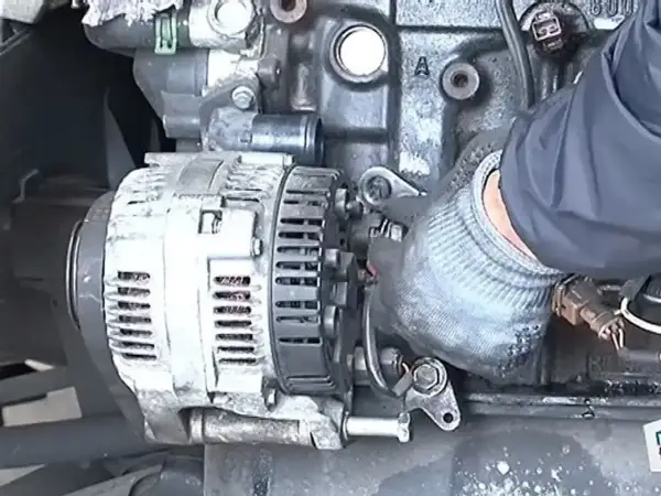 Main d'un mécanicien en gant travaillant sur un alternateur de voiture, étape clé pour apprendre comment changer un alternateur.