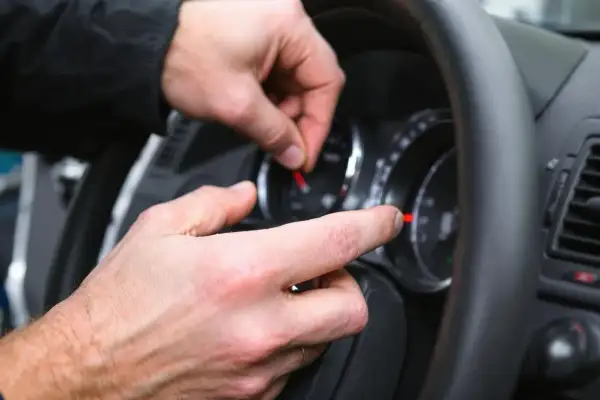 Main d'un mécanicien manipulant le tableau de bord, une astuce pour enlever le voyant airbag.