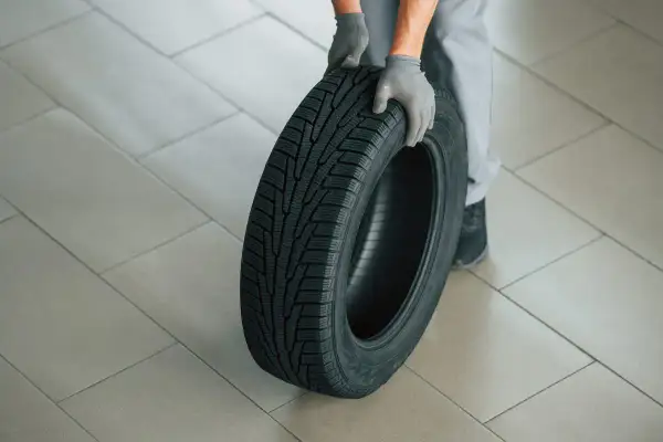 Mains gantées tenant un pneu, le motif de la bande de roulement indique le sens de rotation pneu sans flèche.