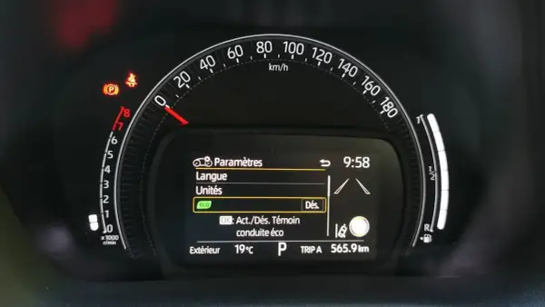 Tableau de bord Toyota Aygo X : voyant pression pneu allumé, menu paramètres affiché. Vitesse 0 km/h, température extérieure 19°C.