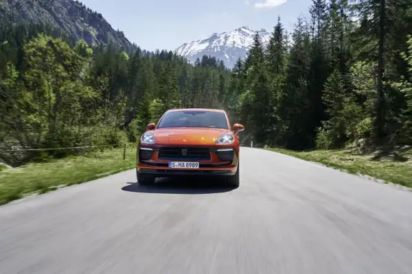 Porsche Macan orange sur une route de montagne, respectant la norme européenne d'émissions.