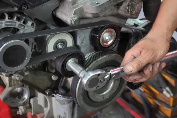 Main d'un mécanicien ajustant la tension courroie accessoire d'un moteur avec une clé à cliquet.