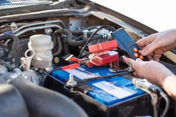 Main d'une personne utilisant un appareil pour tester une batterie de voiture qui se décharge. Les pinces rouges sont connectées à la batterie.