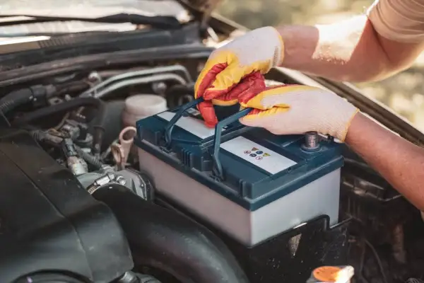 Mains gantées manipulent une batterie de voiture, peut-être pour résoudre un problème de batterie voiture.